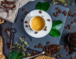 White coffee cup, roasted coffee beans and green leaves on dark background    