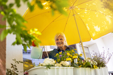 Senior woman taking care of her plants on the balcony 
