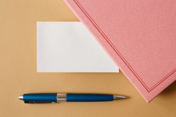 blank white business card, pink diary and metallic blue pen on a brown background flat lay