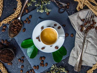 White coffee cup, roasted coffee beans and green leaves on dark background    