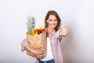 Carrying a healthy bag. Cropped image of beautiful young woman in apron holding paper shopping bag full of fresh vegetables and smiling while showing thumbs up