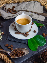 White coffee cup, roasted coffee beans and green leaves on dark background