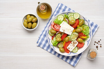 Fototapeta na wymiar Greek salad with feta cheese, tomatoes, cucumbers, lettuce, olives and spices. Traditional greek cuisine. White rustic wooden table
