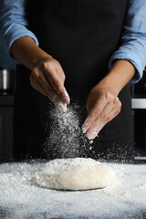 Woman sprinkling flour over dough on table in kitchen, closeup