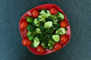 Top view of simple summer salad.Fresh cherry tomatoes, cucumber with dill on the red plate, dark table