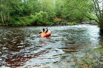 River rafting in summer. A young man rafts in a boat on a river in the wild. Packrafting in...