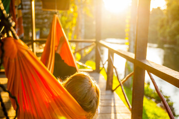 Woman lying in a hammock on the porch of a cabine, enjoying the sunset