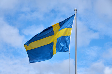 Flag of of Sweden against blue sky with clouds background.