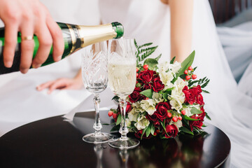 The groom pours champagne for the bride in a glass near a flower bouquet at a wedding