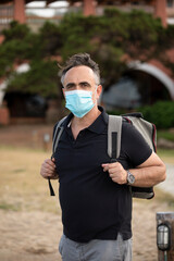 Uomo moro con mascherina facciale protettiva, Maglia nera e zaino in spalla è in vacanza presso...