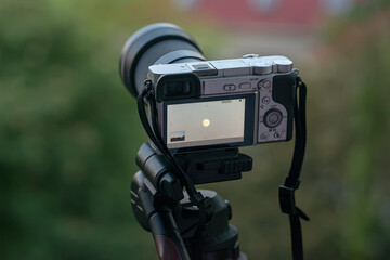 The camera of an unknown model is on a tripod. The camera lens is pointed at the sky at the moon