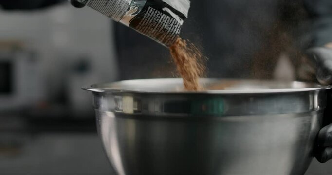 Confectioner pours out the cocoa powder from it's pack to the metal bowl in slow motion, chocolatier makes chocolate sweets and candies, cooking pastry desserts, tabletop foodvideo, 4k 120fps Prores