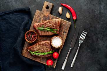 
Two grilled beef steaks with spices on a stone background