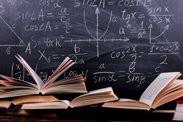 Books are open on the table, against the background of a whitish black board with mathematicsformulas. Concept Teacher's Day, 1st September.