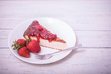 Brownie cheescake with strawberries perfectly arranged on a plate on white wooden table.