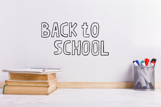 Books, markers, notebook, pencil and glasses on the table against the background of a white board. Copy space.