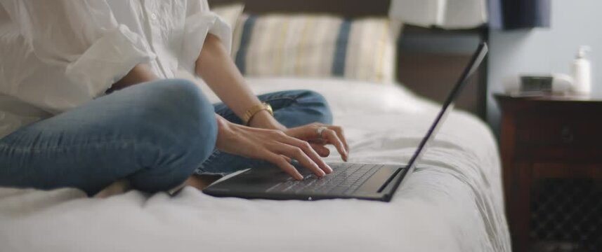 Woman hands typing something on a laptop keyboard in the bedroom. Slow motion, shallow depth of field, tracking shot, BMPCC 4K