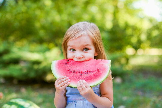 Child eating watermelon in the garden. Kids eat fruit outdoors. Healthy snack for children. 2 years old girl enjoying watermelon.