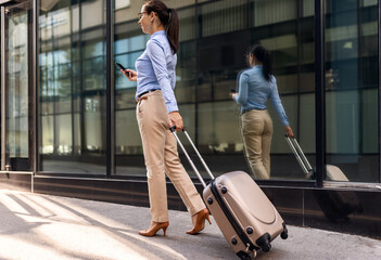 Fototapeta na wymiar Young elegant business woman with luggage walking outdoors in urban city,business trip,travel.