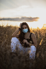 Young woman with black hair wearing a mask for health care in a field at the evening surrounded by...