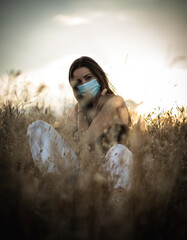 Young woman with black hair wearing a mask for health care in a field at the evening surrounded by...