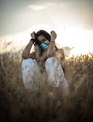 Young woman with black hair wearing a mask for health care in a field at the evening surrounded by...