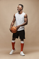 full length photo of a black athletic basketball player in the studio on a beige background wearing a white T-shirt, black shorts, red long socks and white sneakers, he holds the ball and smiles - 356660080
