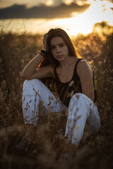 Young woman with black hair in a field at the evening surrounded by plants with the sunset behind