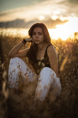 Young woman with black hair in a field at the evening surrounded by plants with the sunset behind