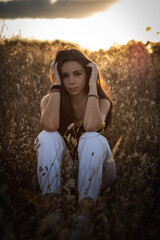 Young woman with black hair in a field at the evening surrounded by plants with the sunset behind
