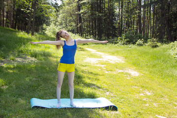 The girl slopes her head to the right standing with arms outstretched. Exercising outdoors.