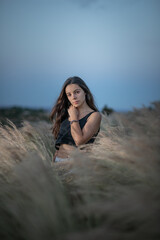 Young woman with long black hair standing between plants looking at the camera during night time after the sunsets with a light hitting her face