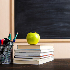 Books, apple, pens, pencils and glasses on a wooden table, against the background of a chalk board. Concept for Teacher's Day, copy space.