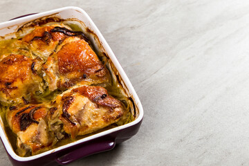 Baked chicken thighs with onions in ceramic form on a stone table, copy space.