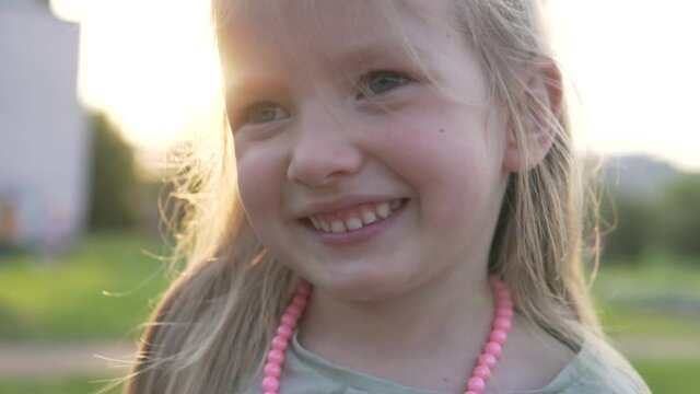 A close-up of a laughing little girl amid a sunset in a summer park.