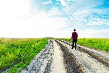 Bright, colorful, juicy, summer landscape. Sun rays are falling on the field. Country road. A man walks along a road leading into the distance.