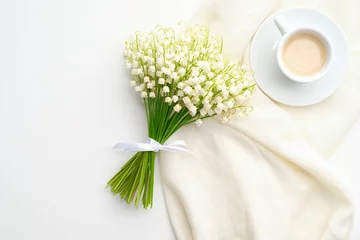 Tragetasche Blumenstrauß Maiglöckchen und morgendliche Kaffeetasse auf weißem Tisch. Frühstück für Muttertag oder Frauentag. Ansicht von oben, flach liegend. © photoguns