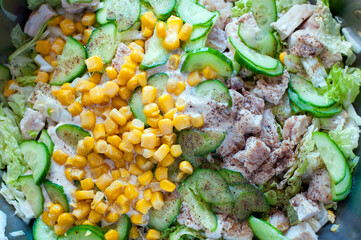 The process of making a summer salad. Sliced ​​vegetables: tomato, cucumber, paprika, green onions, corn and parsley, healthy food
