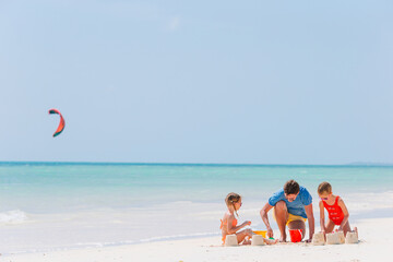 Father and kids making sand castle at tropical beach. Family playing with beach toys