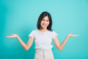 Portrait Asian beautiful young woman standing wear t-shirt, She showing hand to presenting product and looking at the camera, shoot photo in a studio on blue background, There was copy space