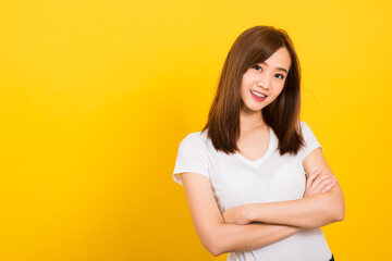 Fototapeta premium Asian happy portrait beautiful cute young woman teen standing wear t-shirt smile her confidence with crossed arms looking to camera isolated, studio shot on yellow background with banner copy space
