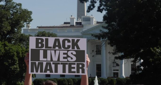 A man holds a BLACK LIVES MATTER protest sign outside the White House.  	