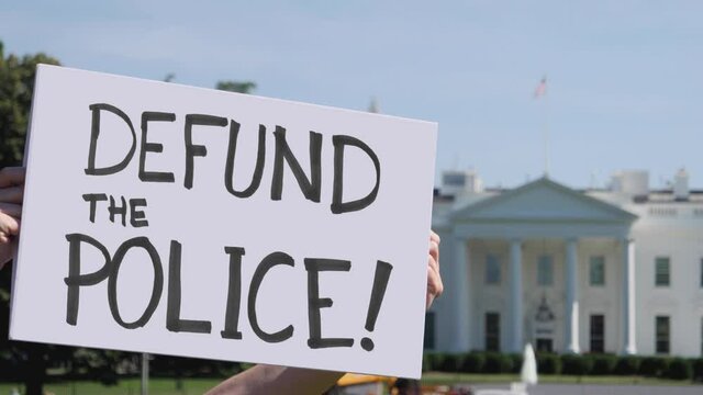 A man holds a handmade DEFUND THE POLICE protest sign outside the White House.  	