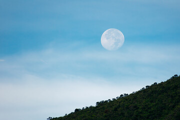 Full moon in the morning with blue sky and a little cloudy hiding in the mountain