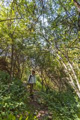 Young adventurer boy with backpack and hat walks through the interior of a Mediterranean forest in Spain. Selective focus.