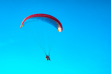 Doubles paragliding against a clear blue sky. A multi-colored papaplan flies in the clear sky closeup.