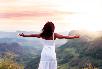 Fototapeta na wymiar Feeling free. Young black girl with arms raised watching the sunset and feeling happy.