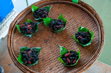 The black juicy mulberry is ripe in the leaves and on the wood floor.