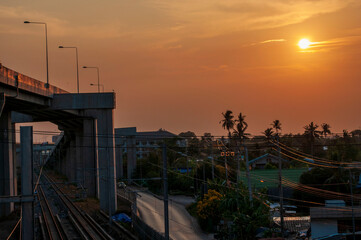 Railway station against beautiful sky at sunrise. Urban landscape with railroad under expressway, colorful of environment with sunrise, trees and green grass. Railway junction.Sun, sky, railroad and e