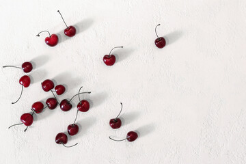 Scattering of ripe cherry berries on white table. Top view, long shadows, copy space